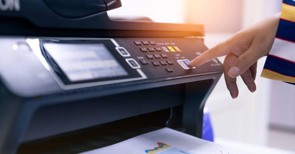 Blurry close-up of the touchscreen and control panel of a Canon multifunction printer with a button pushed by a hand.