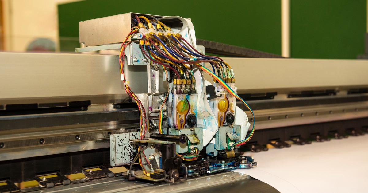 An exposed printer head reveals intricate wiring and several color inks. There is a blank paper loaded on the machine.