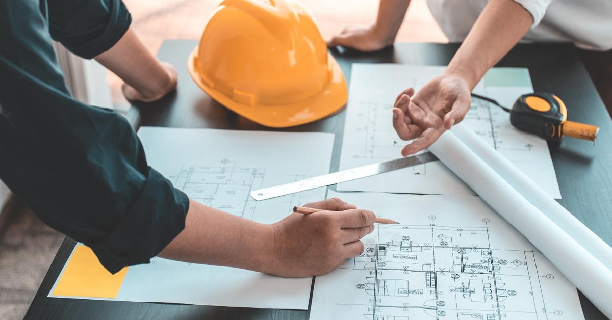 Two architects meet at a worksite to collaborate on building planning details using blueprint schematics.