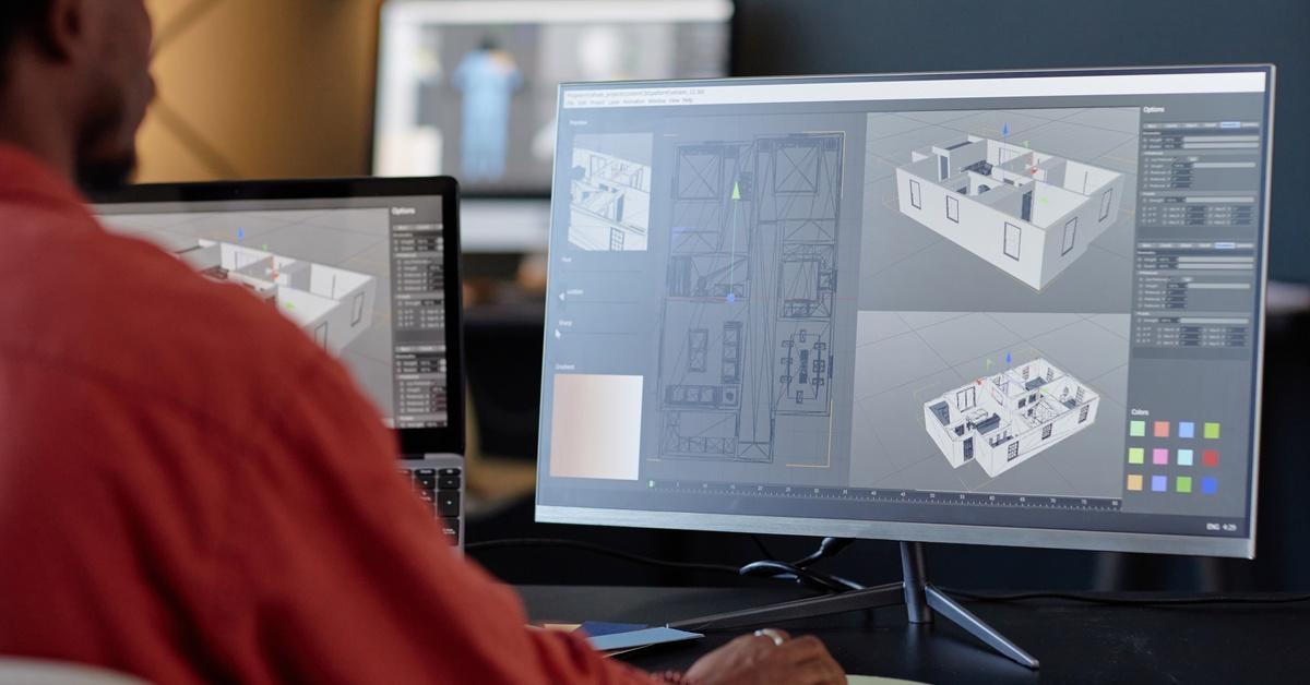  A man works on architectural designs on dual computer screens, viewing 3D building layouts from different angles.