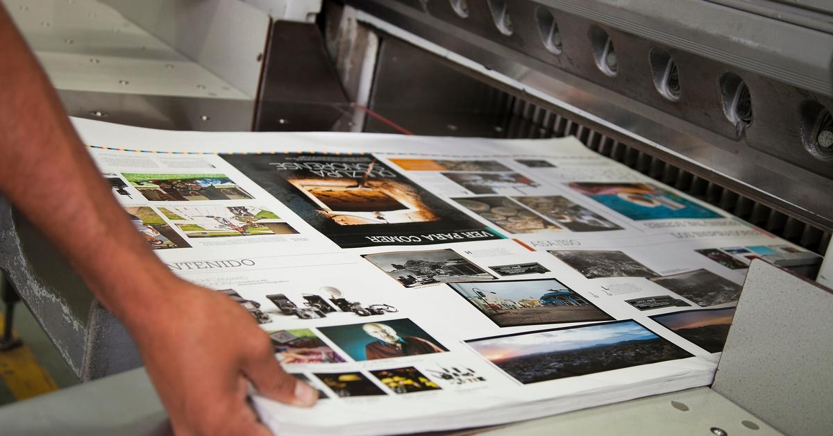 A batch of large prints featuring high-quality images of products, people, and locations emerges from a printer.