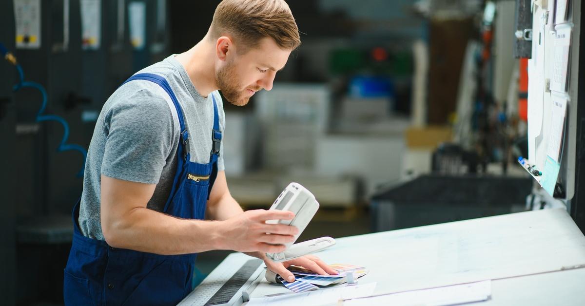 A production line worker uses a small device and reviews color palette references at his workstation.