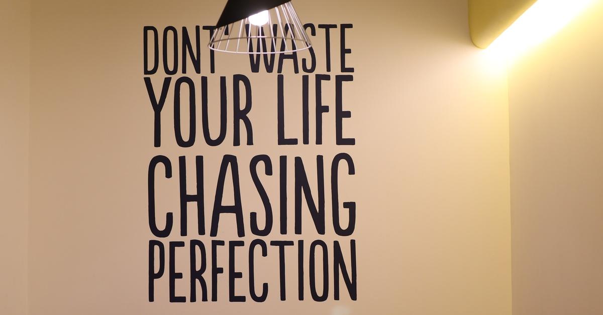 A wall with a hanging light is adorned with a quote that reads: "Don't waste your life chasing perfection."