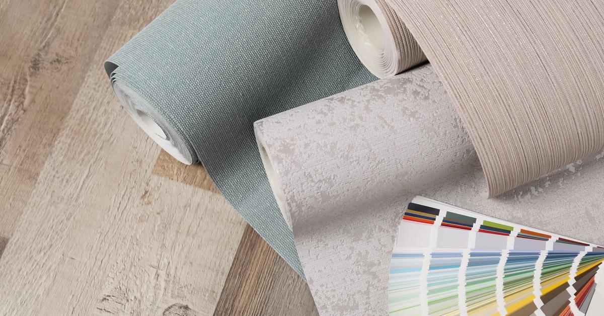 Three rolls of wallpaper made from different materials rest on a wooden surface, alongside a color palette swatch.
