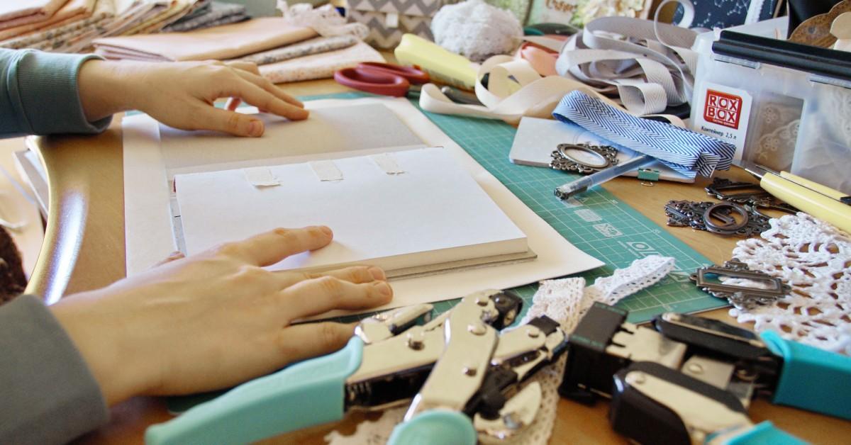 A close-up view of a person at a table with various scrapbooking materials, such as hole punchers and scissors.
