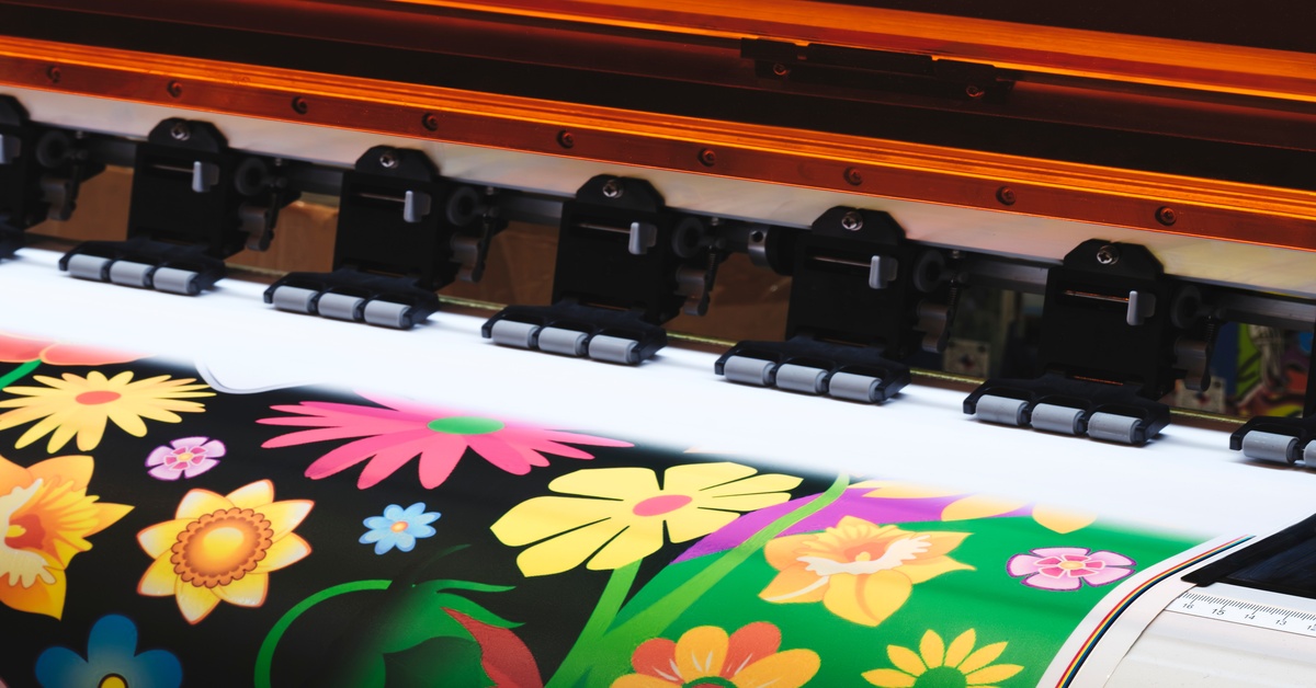 A wide-format printer produces a bright floral design on a roll of material, showing vivid colors moving through print heads.