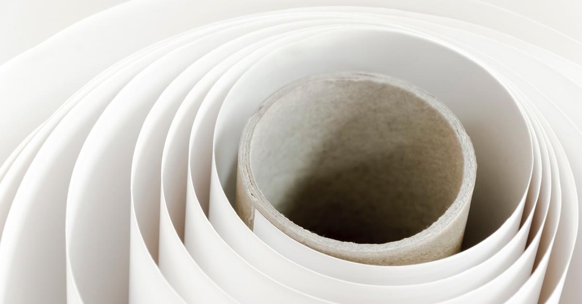 A top view of white paper loosely rolled around a large cardboard tube, illuminated softly from the side.