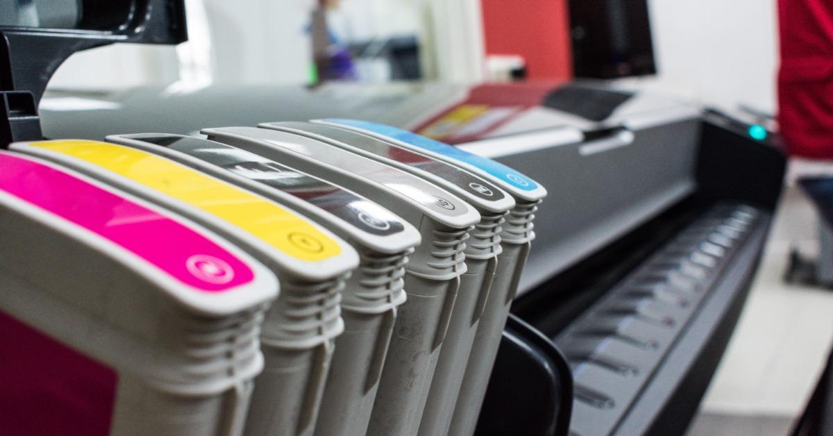 Ink-stained hands holding a removed printer part above a work surface during an inkjet printer repair.